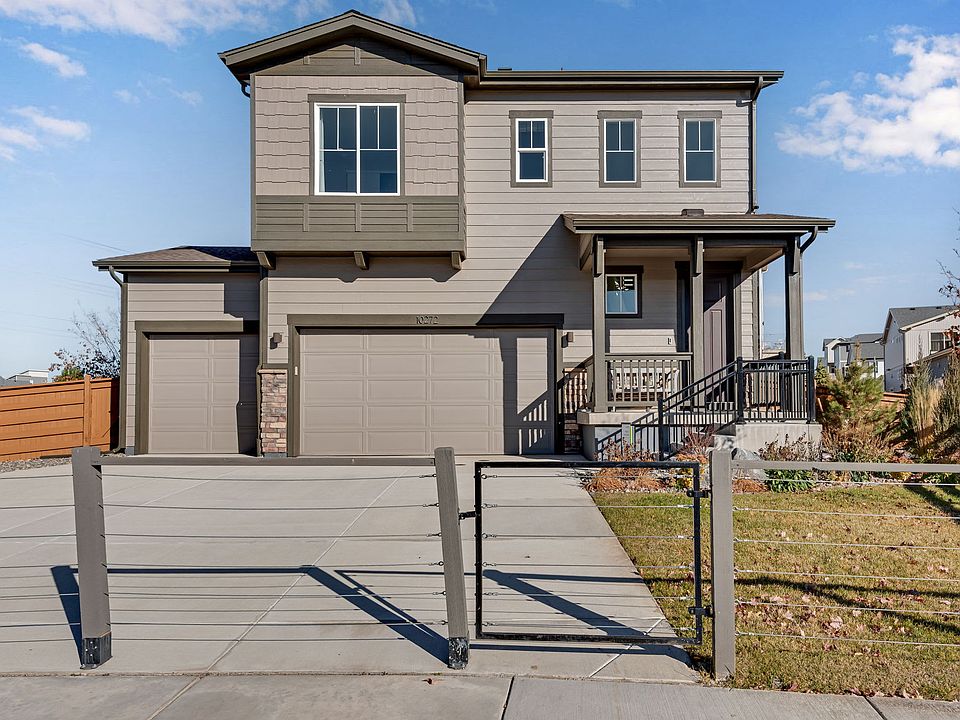A two-story residential house with a gray exterior, a covered porch, and a fenced yard in the foregr
