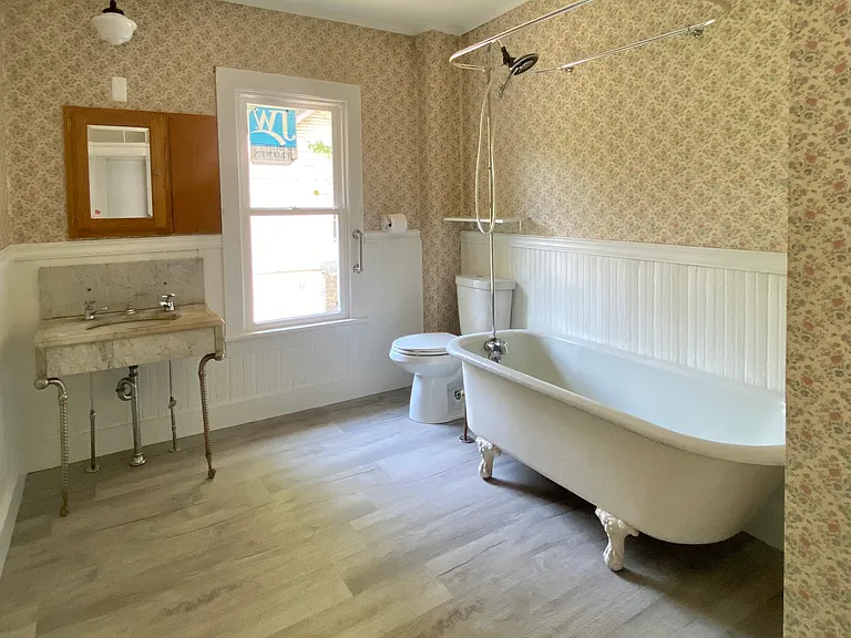 Spacious vintage-inspired bathroom featuring a classic clawfoot soaking tub, pedestal-style marble sink, and newly installed flooring