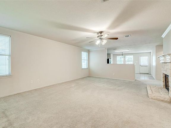 Large family room in this open floor plan has crown molding, ceiling fan with light and a wood burning stone fireplace.