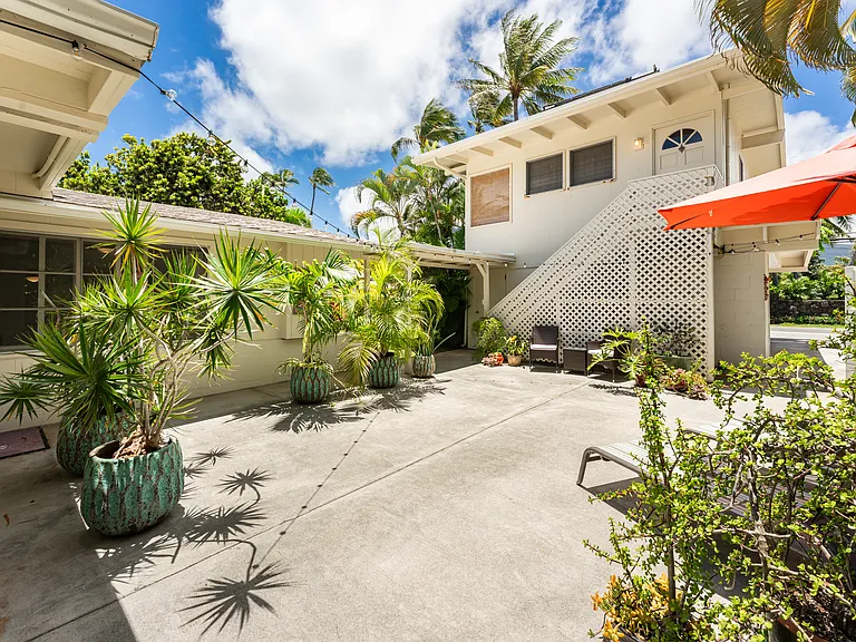 Large private courtyard patio connecting the main home and detached cottage, surrounded by tropical landscaping and outdoor gathering spaces.