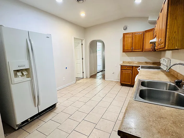 Bright and spacious kitchen with modern appliances, wooden cabinetry, and elegant tiled flooring, offering a welcoming entrance through an archway.