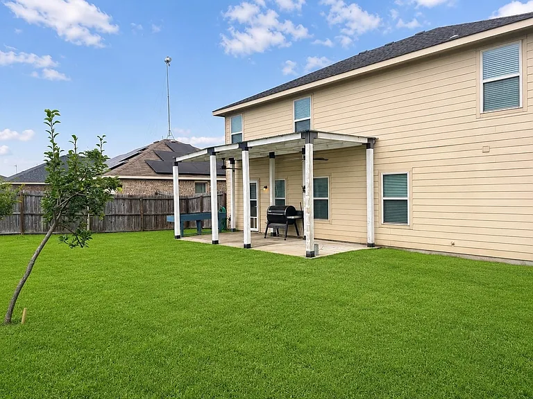 Expansive backyard featuring a lush lawn, a covered patio with dark posts, and tan siding