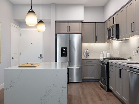 Phase II Signature Collection Kitchen with grey cabinetry, white marble countertops and backsplash, upgraded stainless steel appliances, and hard surface flooring