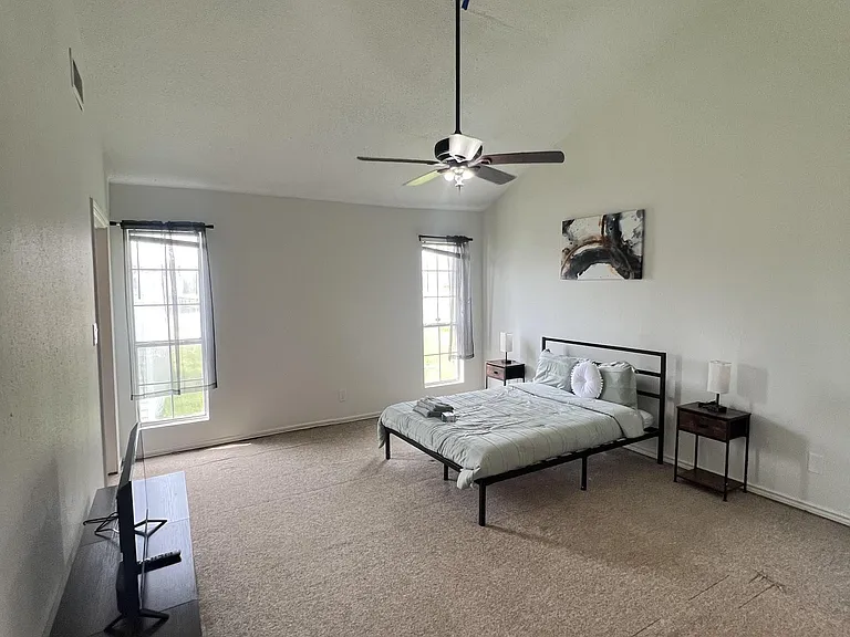 Spacious bedroom with high ceilings, ceiling fan, and two large windows for natural light, plus room for a TV and nightstands