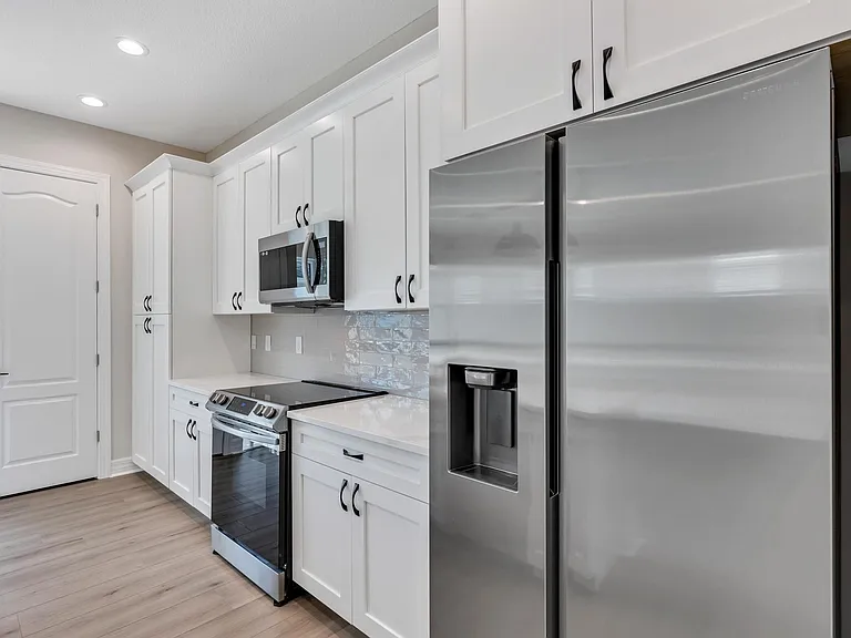View of kitchen fridge, cooking space, cabinets and door to laundry room.