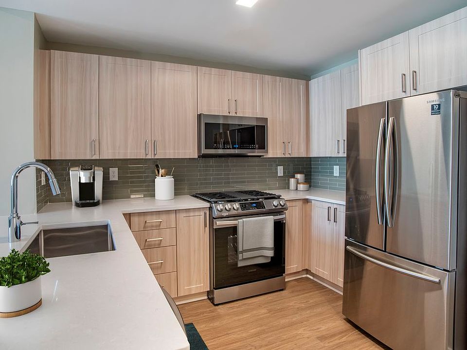 Renovated Package II kitchen with oak cabinetry, white quartz countertops, stainless steel appliances, grey title backsplash, and hard surface flooring