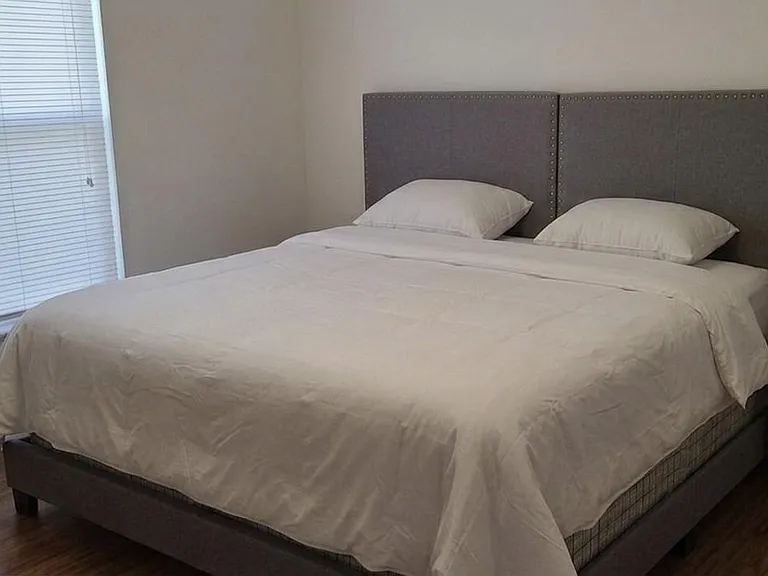 Private bedroom with a King Size bed, upholstered headboard, bedside table and lamp, plus window blinds for light control.