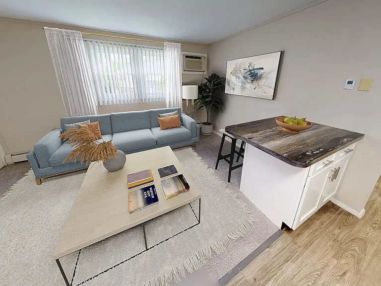 Enjoy a cozy and modern living room in The Dickenson 1-bedroom floor plan at Aspen Chase Apartments, complete with a breakfast bar, plush carpeting, and abundant natural light.