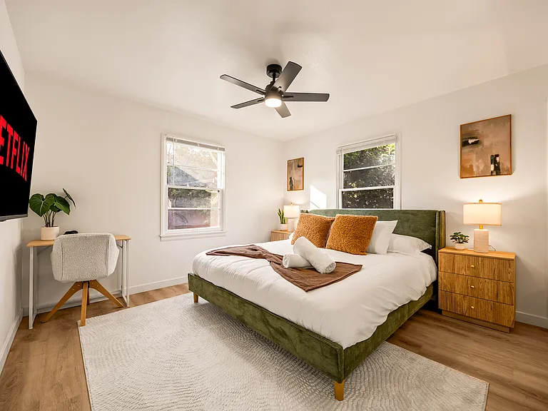 Spacious primary bedroom featuring a king bed, dedicated workspace, ceiling fan, and a calm, relaxing atmosphere ideal for extended stays or working remotely.