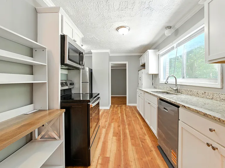 Sunlit Kitchen with stainless steel appliances & crisp white cabinetry. A wide window floods the space with natural light and offers peaceful views while you cook, bake, and gather.