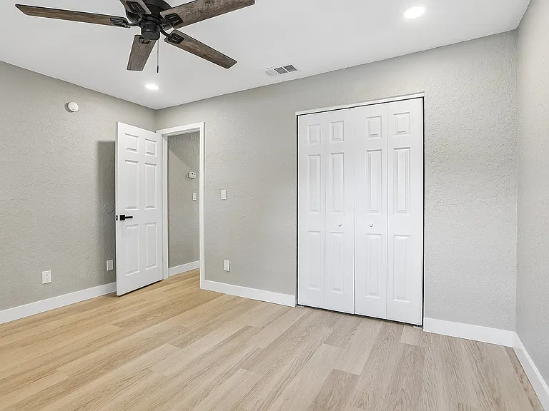 Spacious bedroom with modern ceiling fan, elegant wood floors, and ample closet space in a chic apartment.