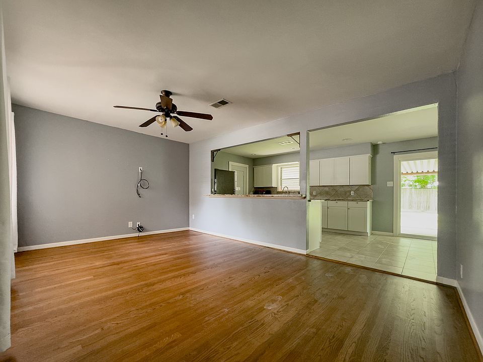 Spacious front living room with original hardwood floors, ceiling fan, and open sightlines into the kitchen and dining areas. Natural flow from front entry to backyard patio through sliding glass doors.