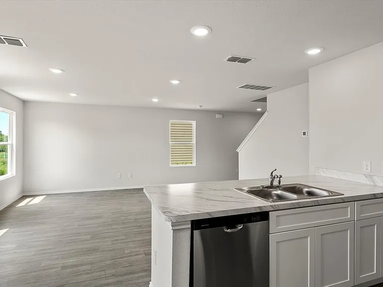 Kitchen island featuring a double basin stainless steel sink, stainless steel dishwasher, and a light-toned
 countertop