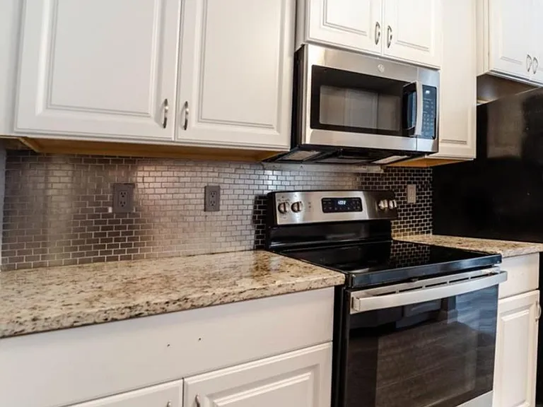 Updated kitchen with white cabinetry, granite-style counters, tile backsplash, and stainless steel range with microwave.