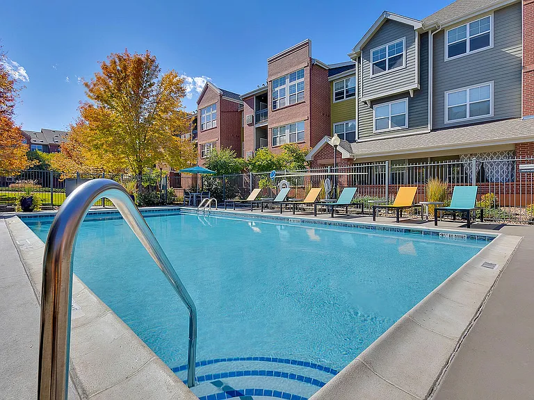 Inviting outdoor pool with colorful lounge chairs at a modern apartment complex, surrounded by lush autumn trees.