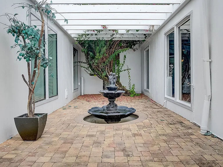 Charming courtyard with a serene stone fountain surrounded by lush greenery and sleek modern design.
