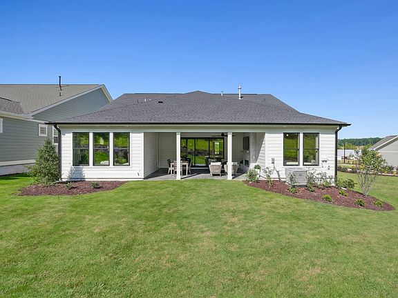 A well-manicured lawn surrounds a modern, single-story house with a covered porch and large windows,