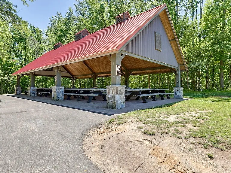 Covered outdoor pavilion with picnic tables, stone supports, and a paved approachideal for gatherings and cookouts.