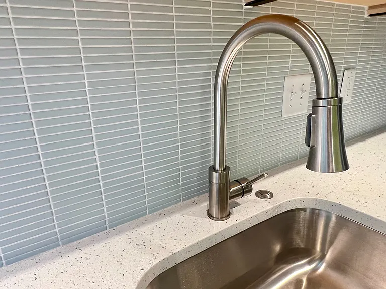 Detail of tile, quartz countertop, gooseneck faucet with built in detachable nozzle, garbage disposal.