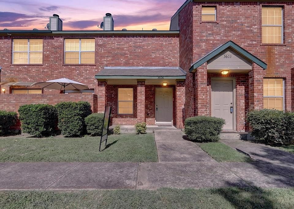 Brick-clad townhome exterior with a covered entry, established landscaping, and a paver walkway