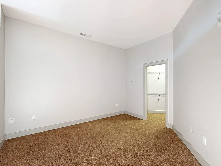 Spacious apartment bedroom with large closet and plush carpet flooring.