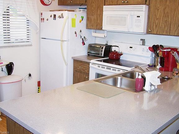 View of the kitchen shows the kitchen window, white appliances, cabinetry, stainless sink, and large countertop.