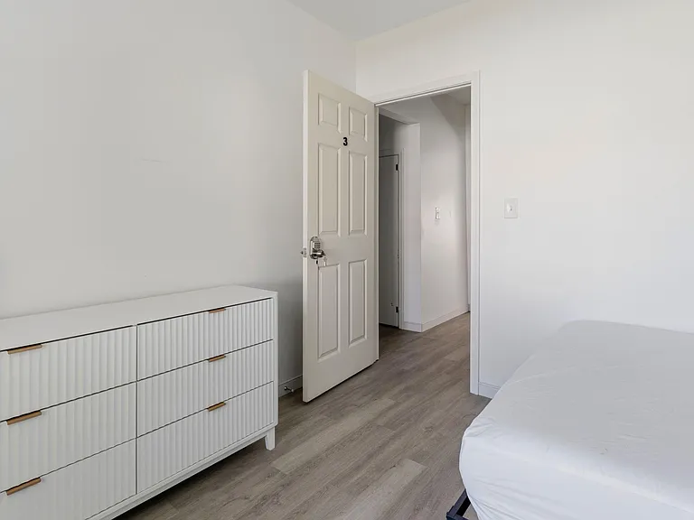Bedroom features durable wood-look flooring, a dresser for storage, and an easy-access layout with entry to the hall.