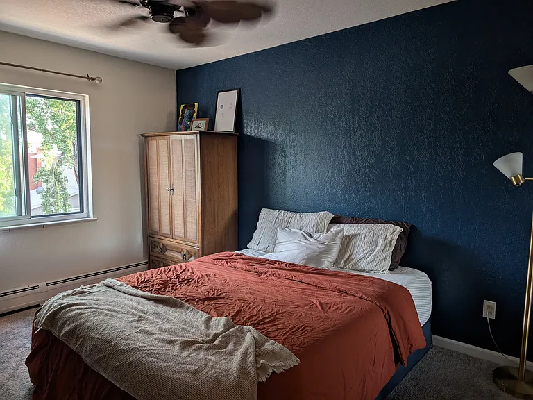 Bedroom with a large window and natural light. One full wall of mirrored doors to the bedroom closet, which includes custom shelving and hanging racks.