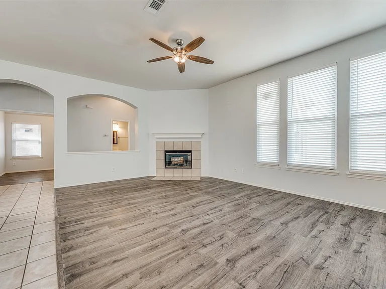 Spacious living area featuring wood-finish flooring, a tiled fireplace with hearth, and a ceiling fan