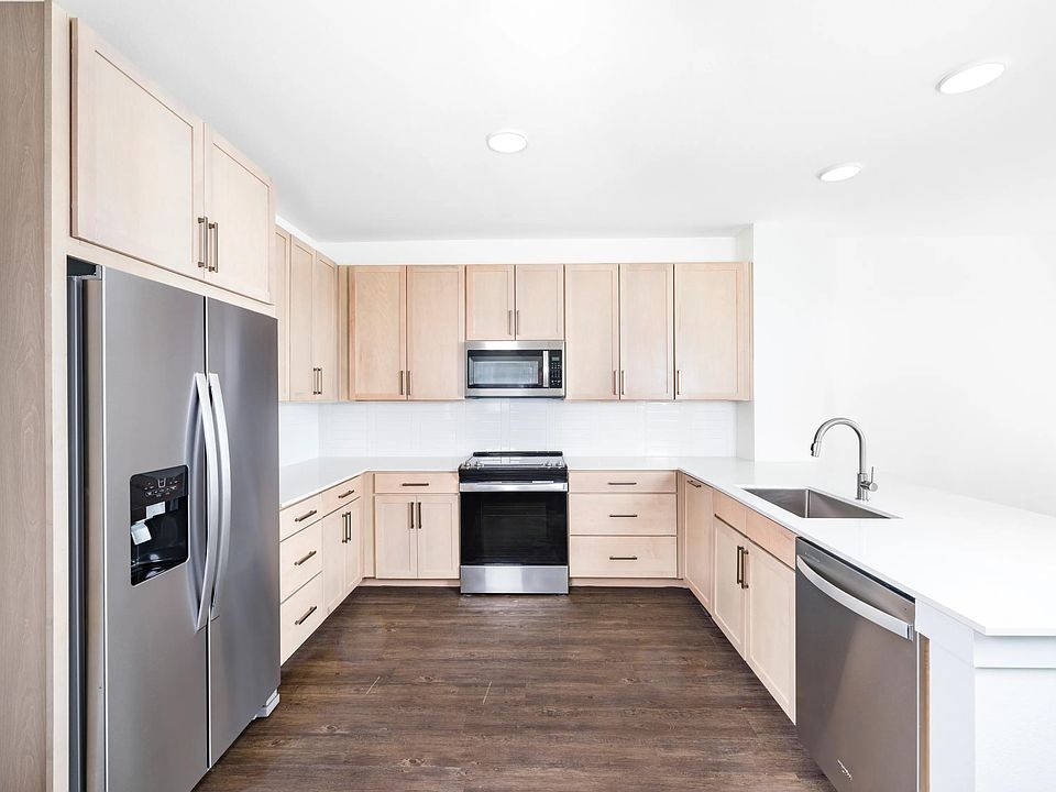 U-shaped kitchen with light wood cabinetry, quartz countertops, and stainless steel appliances arranged for efficient cooking and everyday use.
