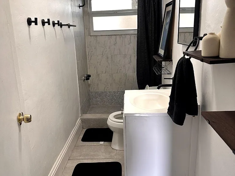 Streamlined full bath with tiled tub/shower, frosted window for privacy, and a recessed vanity mirror and open shelving.