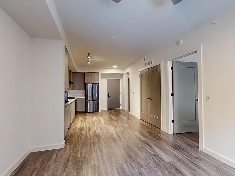 Apartment kitchen with black stainless steel appliances, dining and living room with wood-style flooring.