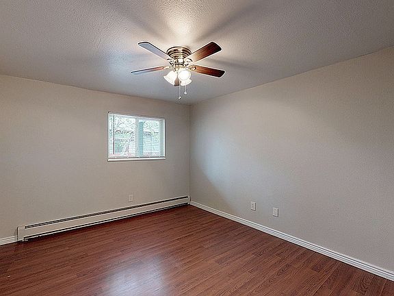 Bright and airy room featuring sleek hardwood flooring, a modern ceiling fan, and a large window letting in natural light.
