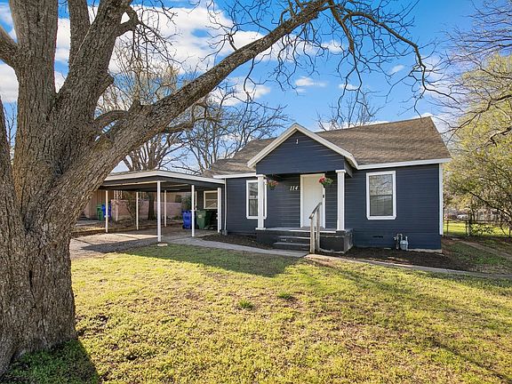Shady front yard with mature pecan tree, paved driveway with adjoining carport.