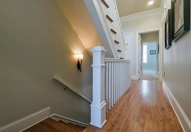 Hardwood flooring extending through a hallway with white baseboards and crown molding