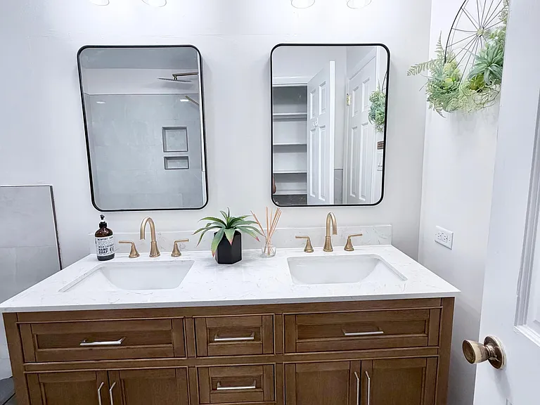 Bathroom vanity offers a double-sink setup with ample drawer storage, sleek counters, and updated lighting with two mirrors.