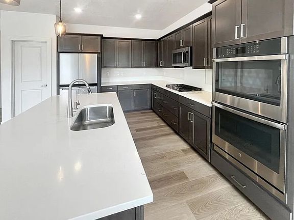 Open kitchen with quartz countertops, island, stainless appliances, and double oven