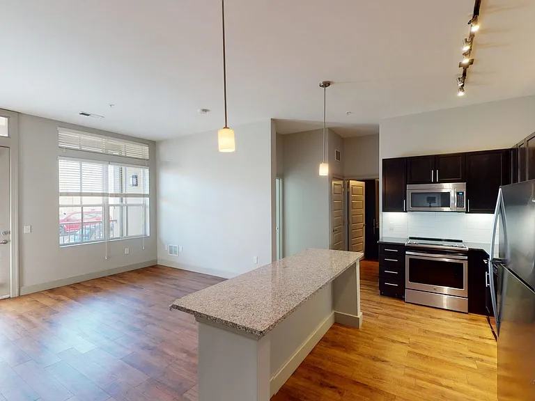 Apartment kitchen with stainless steel appliances, dining and living room with wood-style flooring.