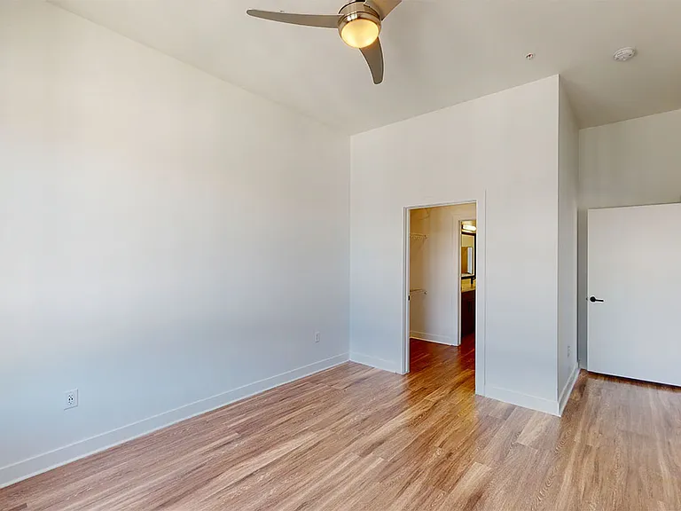 Spacious apartment bedroom with large closet, attached bathroom and wood style flooring.