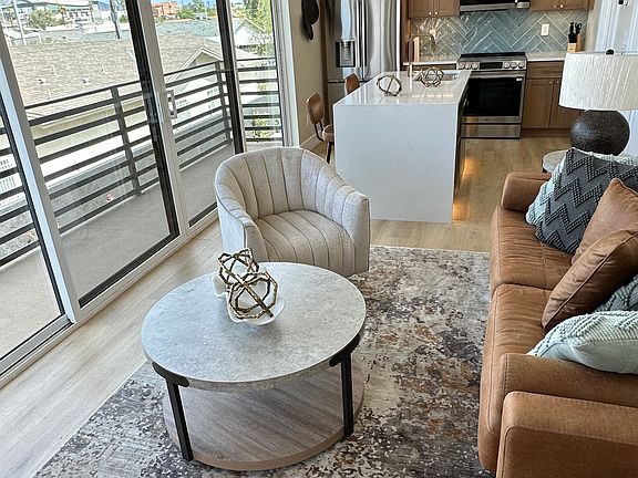 Sunlit furnished living area with large windows and balcony access.