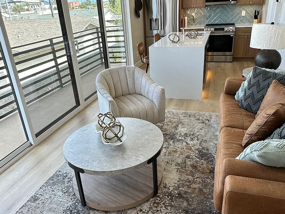 Sunlit furnished living area with large windows and balcony access.
