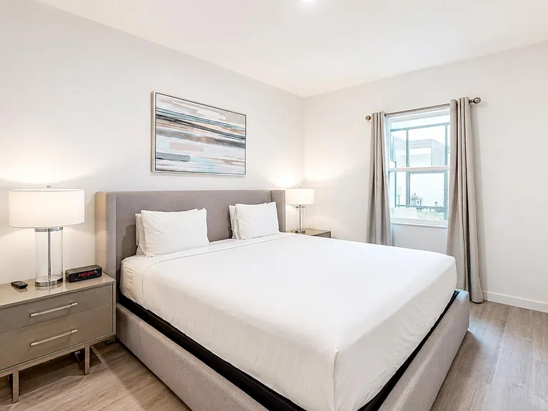 Well-appointed bedroom with a cushioned bed, nightstands with lamps, and a window with curtains for natural light.