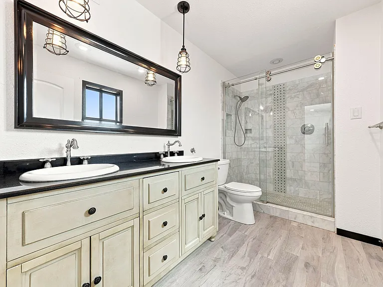Spacious bath features a double-sink vanity with ample storage and a glass-enclosed tiled shower.