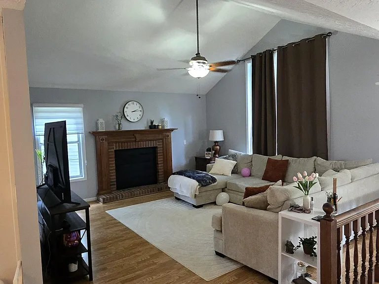 Spacious living room with hardwood floors, a brick fireplace, ceiling fan, and sectional seating area.