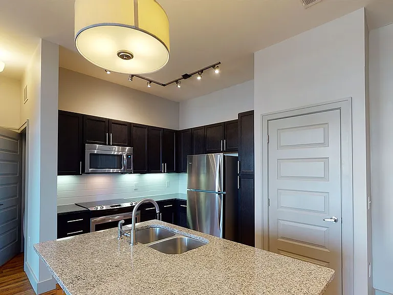 Apartment kitchen with stainless steel appliances, granite countertops and wood-style flooring.
