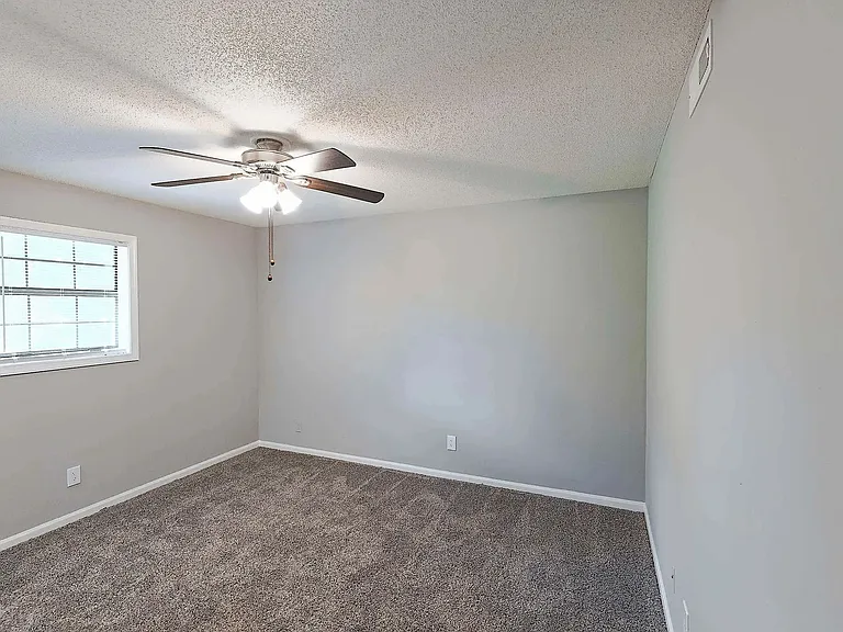 Spacious bedroom with plush carpeting, ceiling fan, and natural light