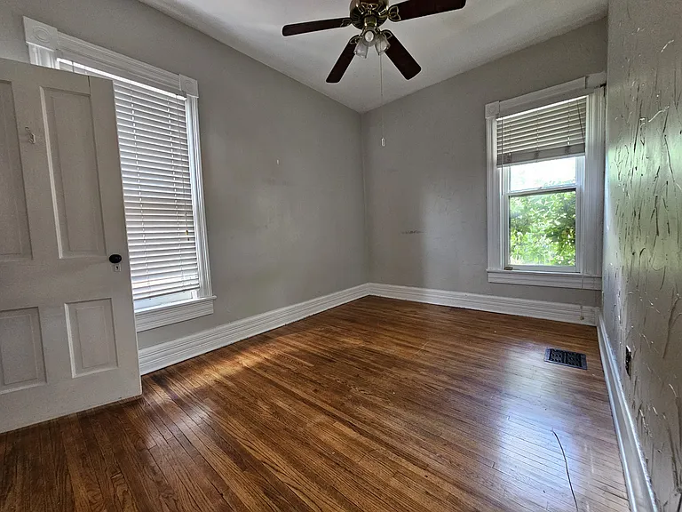 Secondary bedroom with rustic wooden flooring and large windows.