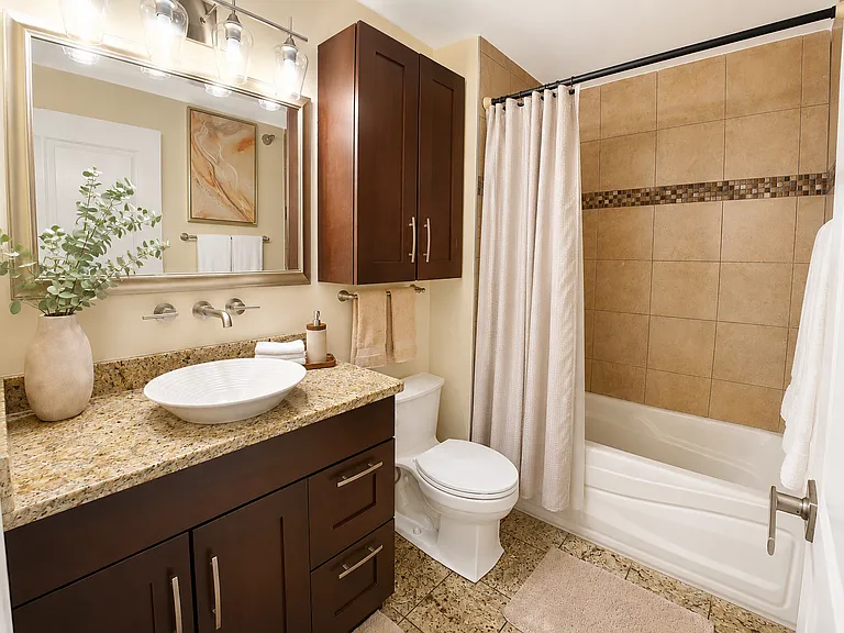 Elegant bathroom featuring a stylish vessel sink resting beautifully atop luxurious marble by the sink. The space is completed with rich espresso cabinetry for convenient storage, modern lighting, and warm, neutral tiling throughout.