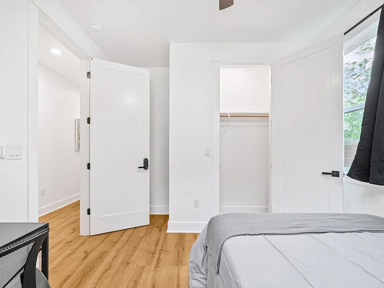 Bedroom with wood-look floors, open closet storage, and a large window for natural light and fresh air.