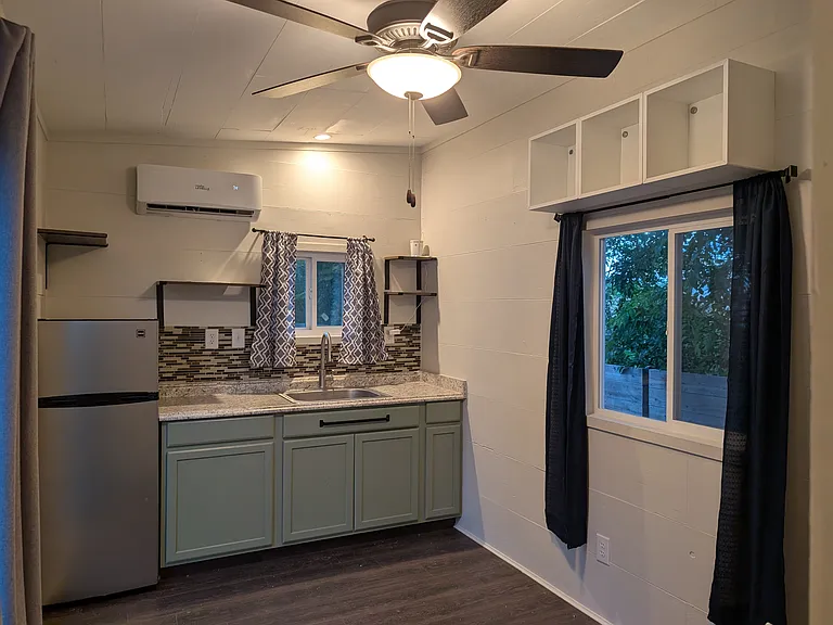 Kitchen with full refrigerator, hot plate, large sink, ceramic tile backsplash, and lots of cabinet and shelf space. Mini split provides heating and cooling. Kitchen / living area ceiling fan to keep air flowing throughout the home.